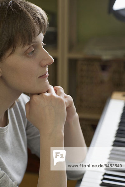 Eine Frau  die sich auf ein Klavier stützt und nachdenklich aussieht.