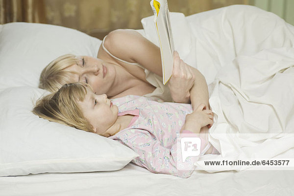 Eine Mutter und ihre kleine Tochter liegen im Bett und lesen ein Buch.