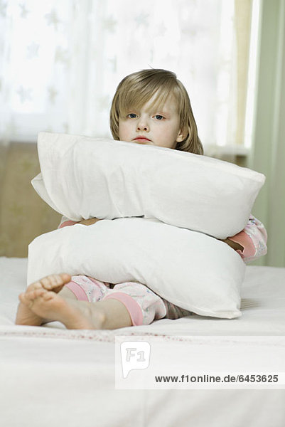 Ein traurig aussehendes kleines Mädchen  das ein Kissen drückt.
