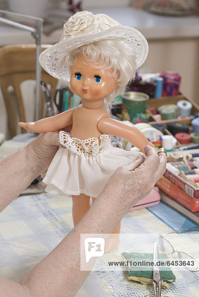 Eine ältere Frau hält eine Puppe neben einem Nähzeug.