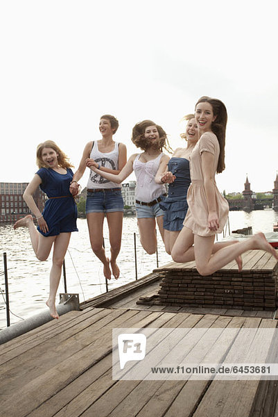 Five young female friends jumping in the air on a jetty next to the Spree  Berlin  Germany