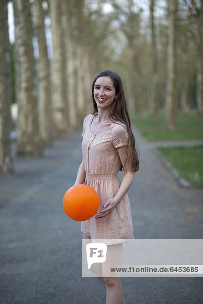 A young woman holding an orange ball  standing in a park