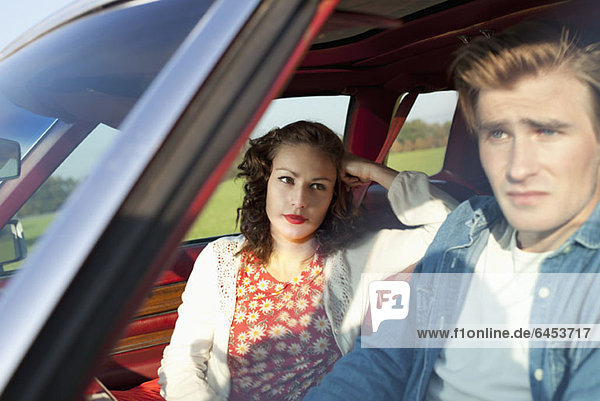 A pretty rockabilly girl looking at her boyfriend in irritation while sitting in vintage car