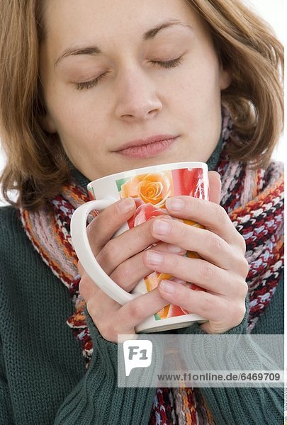 Junge Frau wärmt sich die Hände an einem Becher *** Local Caption ***