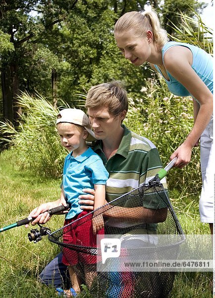 1224898 outdoor park day summer couple family young woman blonde ponytail man young dark haired blouse blue blouses boy child 0-5 cap son father mother parents 25-30 hold fishing rod fish net vacation holdays recreation stand kneel smile smiling profile profiles close up vertical