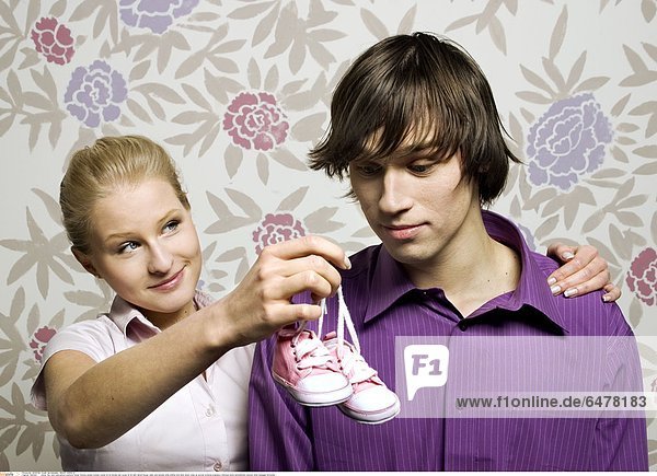 1225352 indoor flat room wall pattern patterns flower flowers people woman couple 25-30 blonde man young 30-35 dark haired blouse violet pink blouses smile smiling hold shoe shoes close up portrait symbole pregnancy embrace show astonishment surprise mime message horizontal