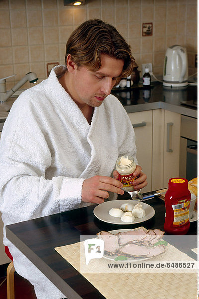 1222039 indoor flat kitchen young man 25-30 dark haired beard white dressing gown sit table prepare meal food breakfast egg egges pork meat ham ketchup garnish plate plates close up vertical