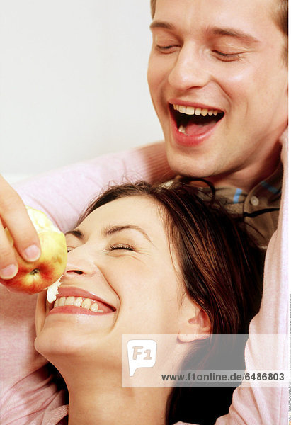 1218811 indoor flat room man woman couple young 25-30 brunette fair haired sit rest relax close up portrait smile smiling eat apple hold eye eyes close diet health bit emotions joy feed embrace rest relax vertical
