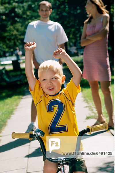 1236495 outdoor summer park spring day people child boy 0-5 fair haired rest relax blouse yellow sit ride bike close up mother brunette woman young 25-30 long vertical blur father family man couple 30-35 dark stand dress pink blouses white