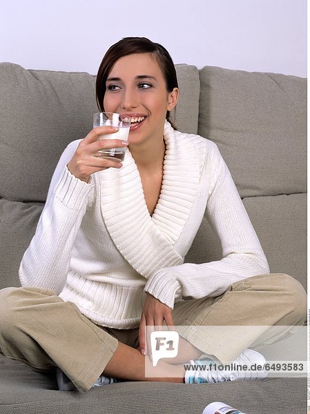 1239370 indoor flat room sit rest relax sofa people woman brunette young 20-25 girl sweater white trousers beige drink milk smile smiling glass hold vertical