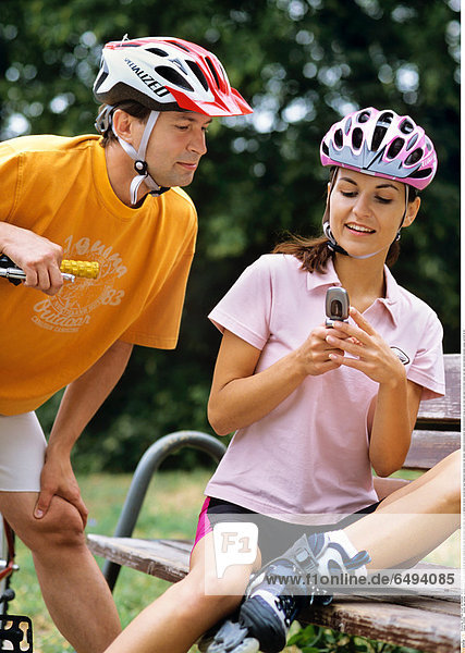 1239289 outdoor day summer vacation people woman young 20-25 girl smile smiling blouse pink shorts black park relax rest sport helmet sit bench vertical hold hand telephone mobile phone cell cellular cellphone communication telecommunication close up sms mms read send write bike couple man dark haired helmets blouses orange vertical 25-30