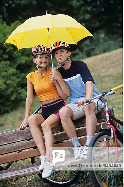 1239295 outdoor day summer vacation people woman young 20-25 girl smile smiling blouse orange shorts black park relax rest sport helmet sit bench man couple dark haired helmets hold yellow umbrella fun play vertical blouses blue bike bikes ride 25-30