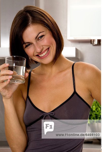 1247196 indoor flat kitchen people woman young 25-30 brunette close up blouse grey hand hold glass water drink diet smile smiling vertical