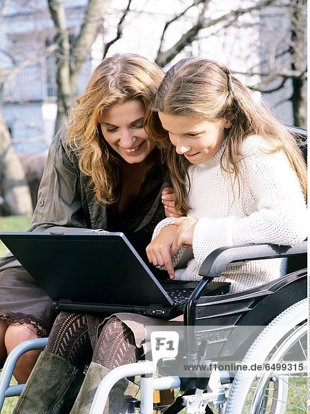 1249074 outdoor people mother daughter woman 30-35 child girl 5-10 10-15 blonde smile smiling laptop notebook personal internet communication compter veeling chair disablement disability physically handicapped vertical