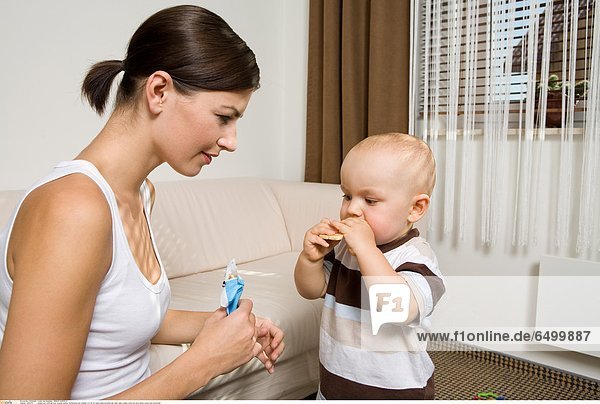 1252276 people two child girl boy woman mother motherhood son douther 0-5 25-30 years adult brunette eat feed cake cookie couch sit sofa indoor living-room horizontal