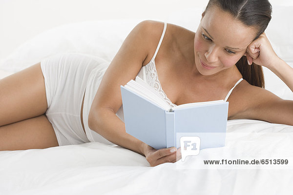 Woman in underwear reading book while laying on bed