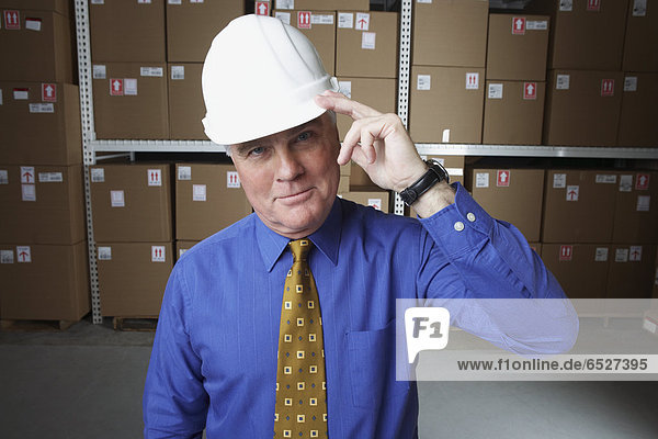 Businessman wearing hard hat and saluting in warehouse