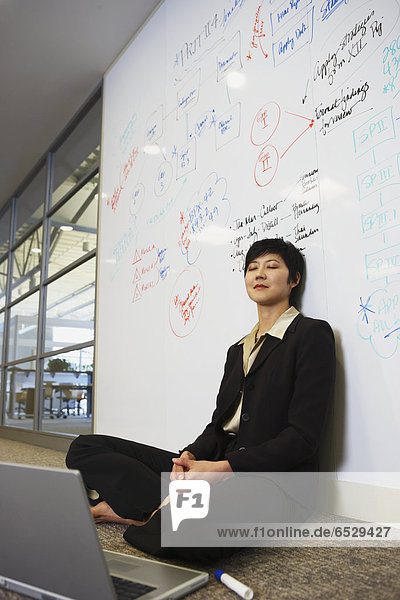Asian businesswoman with laptop on floor in front of whiteboard wall
