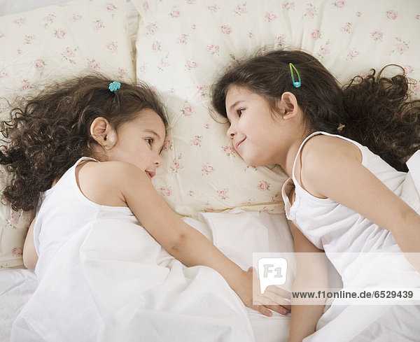 Two young Hispanic sisters lying in bed