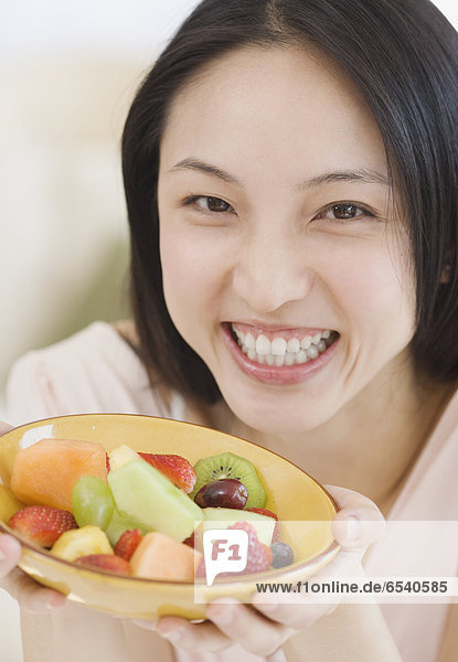 Asian woman holding bowl of fruit