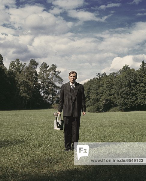 Portrait of man standing on meadow and holding watering can
