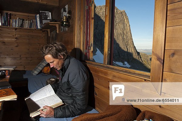 Mid adult man sitting in mountain cabin and reading book