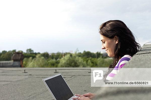 Young woman sitting on roof and using laptop