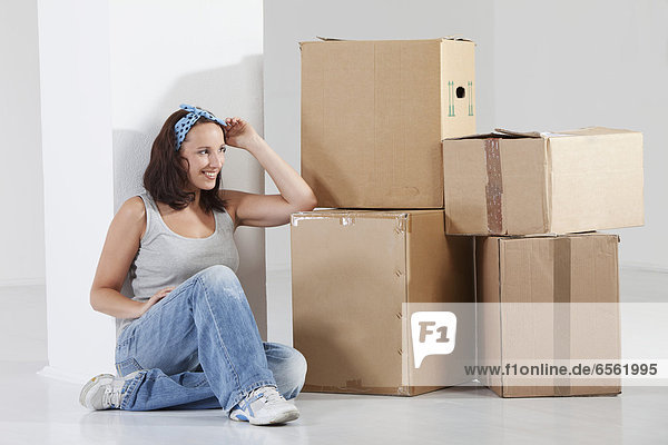 Young woman sitting by cardboard box  smiling
