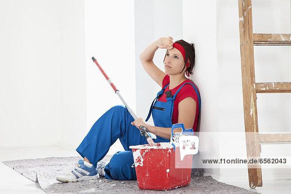 Young woman tired  sitting with paint tin and brush