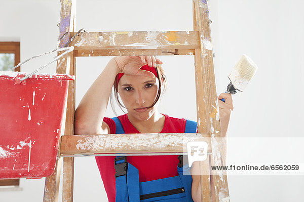 Young woman standing on step ladder with paint brush
