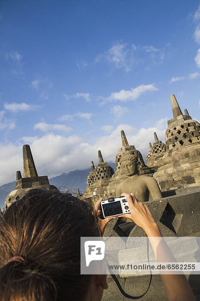 Indonesia  Young woman taking photo of Buddha statue at Borobudur Temple