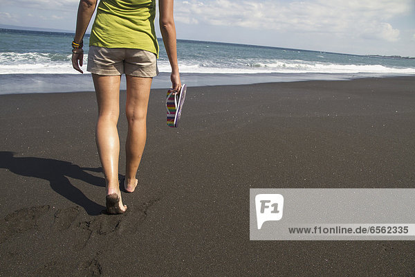 Indonesien. Junge Frau läuft auf schwarzem Sand