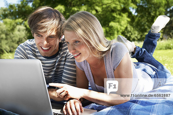 Germany  Cologne  Young couple using laptop in meadow  smiling