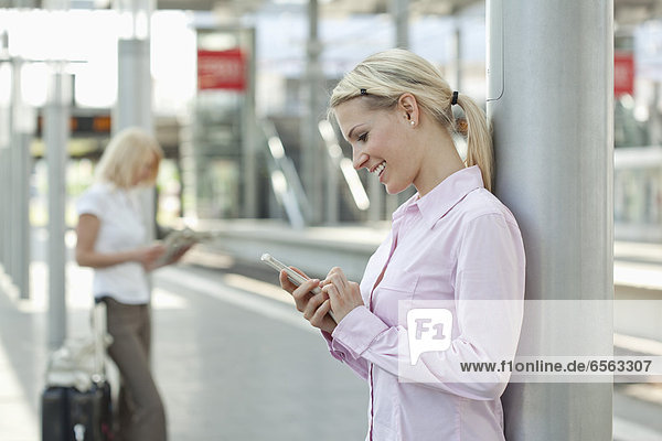 Geschäftsfrau mit Smartphone  eine andere Frau liest Zeitung im Hintergrund