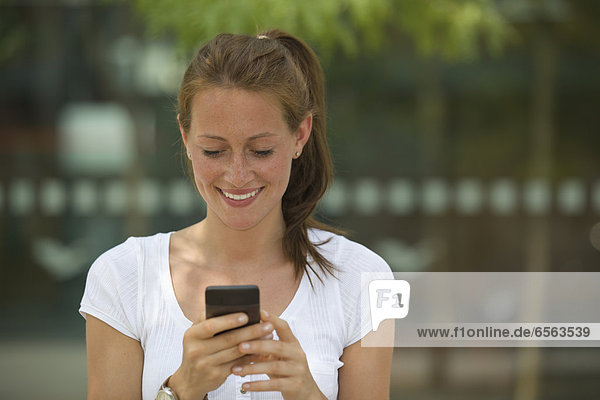 Germany  North Rhine Westphalia  Cologne  Young woman using smart phone  smiling