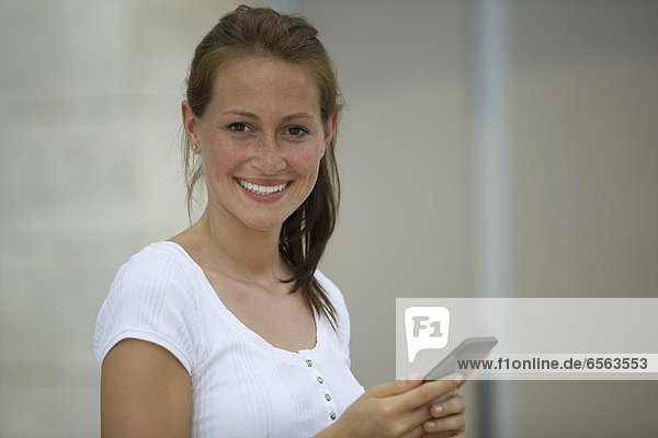 Deutschland  Nordrhein-Westfalen  Köln  Junge Frau mit Smartphone  lächelnd  Portrait