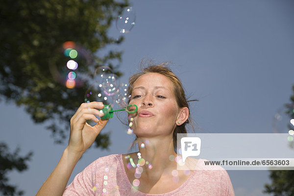 Germany  North Rhine Westphalia  Cologne  Young woman blowing soap bubbles