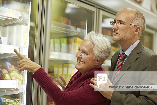Germany  Cologne  Mature couple choosing from freezer in supermarket