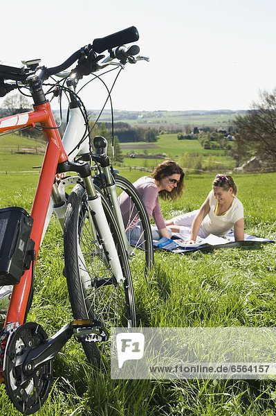 Mature women sitting on grass and looking at map  electric bicycle in foreground