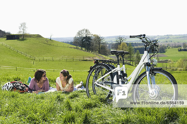 Mature women lying on grass  electric bicycle in foreground