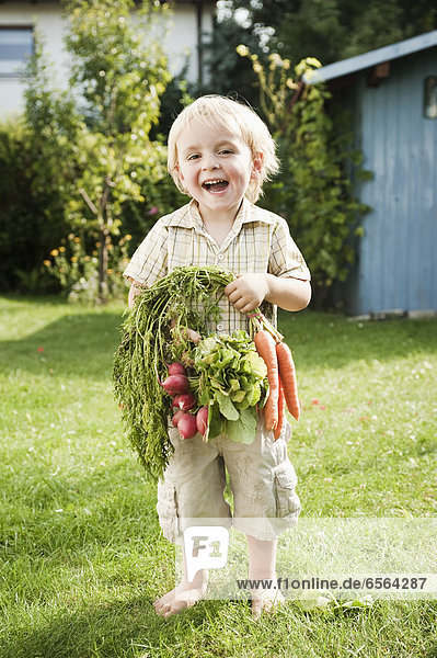 Junge mit Karotten und Radieschen  lächelnd  Portrait