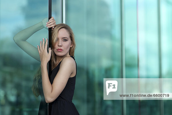 Young woman in a black dress posing in front of a green glass facade