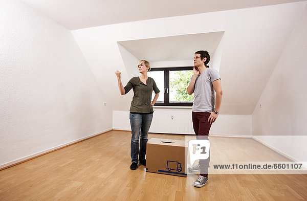 Young couple carrying the first moving box into the empty living room in a new apartment