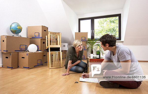 Young couple sitting in an empty room in a new apartment and reading the lease