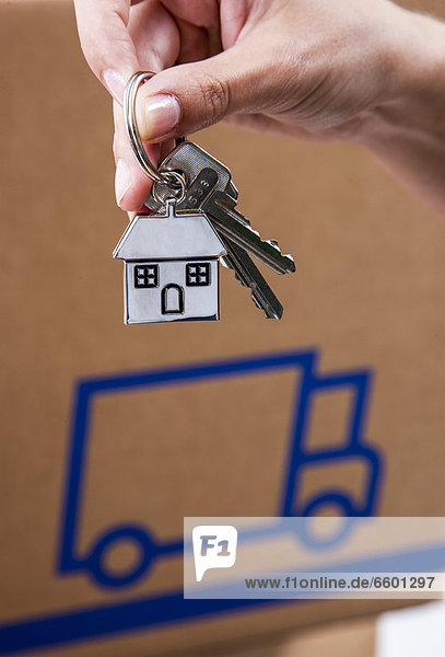 Hand holding house keys with a metal key tag shaped like a house  moving boxes at the back