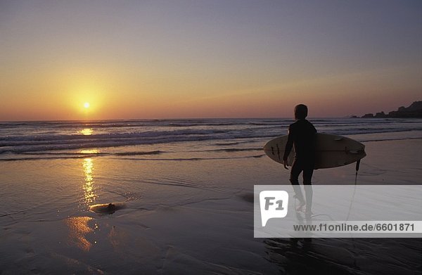 Silhouetted Surfer On Sandy Beach At Sunset