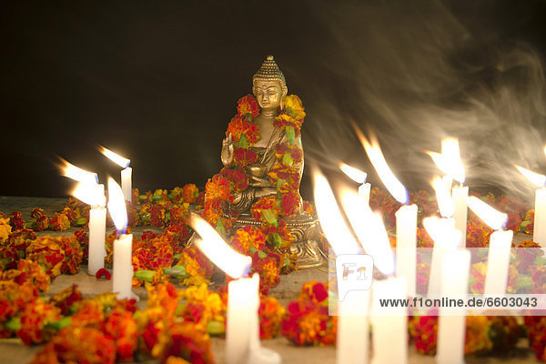 A figure of Buddha Shakyamuni is decorated with leis or garlands and is surrounded by burning candles  on the banks of the Ganges  Varanasi  Uttar Pradesh  India  Asia