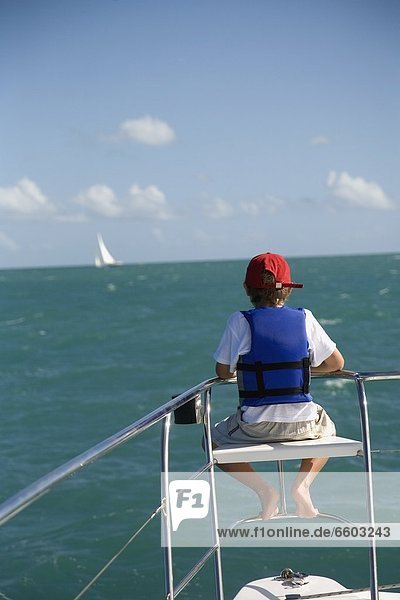Boy In Life Vest Sitting On Edge Of Sailboat