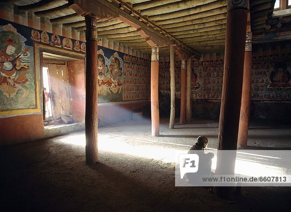 Old Man Praying In Tsemo Monastery With Ray Of Light Coming Through Doorway