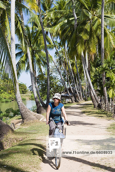 Young Woman Cycling Along The Main Road On Don Khon Island.